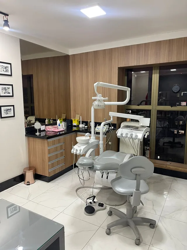 Consultório da Dra. Greicy, com cadeira odontológica cinza e painel de madeira