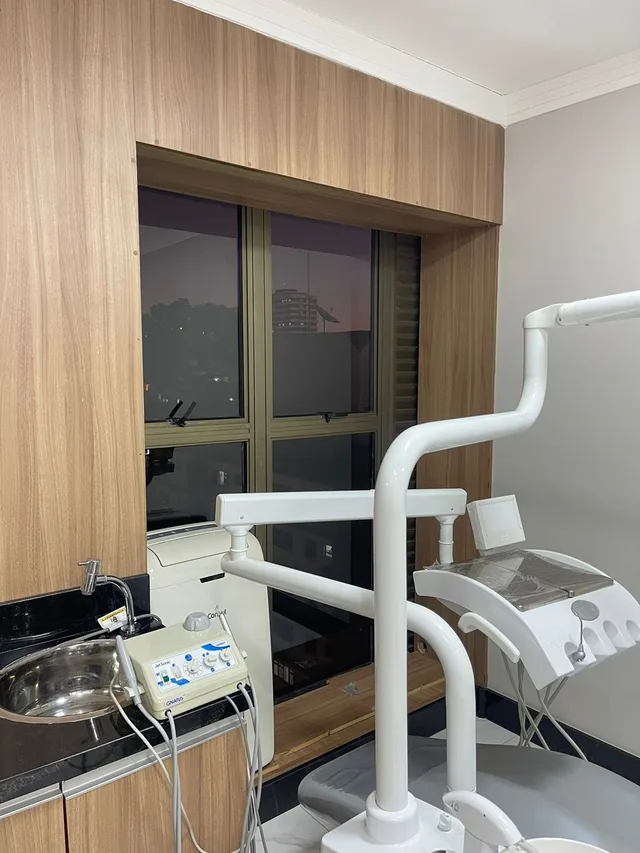 Cadeira odontológica com refletor junto à janela com painel de madeira