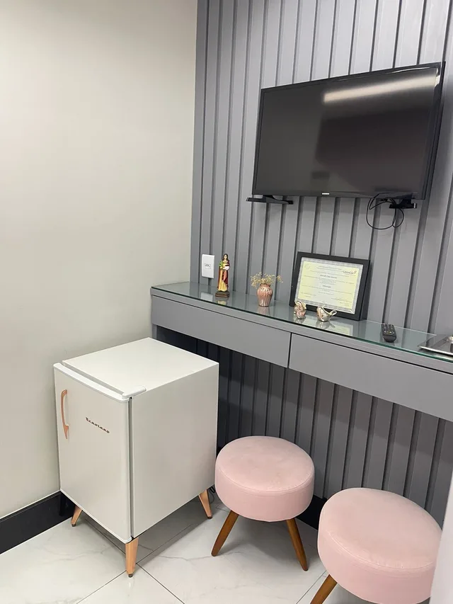 Recepção com painel ripado cinza, televisão e banquetas rosa